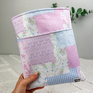 May include: A rectangular fabric pouch featuring a patchwork design of various floral, polka dot, and gingham patterns in shades of light blue, lavender, and white. A small white fabric label with the black text Patchy Berry is attached.