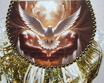 May include: A round decorative piece featuring a dove with outstretched wings, set against a background of hands. The image is framed with gold beads and a gold handle. Gold and white ribbons and tinsel add to the decorative design.