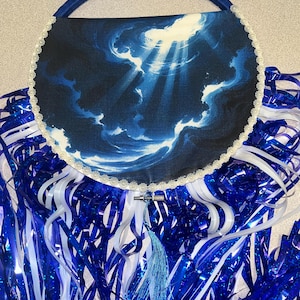 May include: A round, blue handbag with a handle. The bag features a celestial design with clouds and light rays. It is trimmed with white lace and a blue tassel. Blue and white streamers are below the bag.