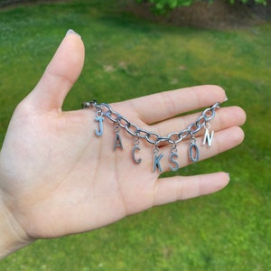 May include: A silver chain bracelet with letter charms spelling out the name "JACKSON".