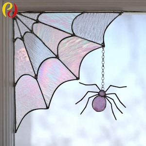 May include: A stained glass spider web corner decoration with a hanging spider. The web is made of iridescent glass with black lines. The spider is purple with black legs and is suspended by a chain. A Halloween decoration.