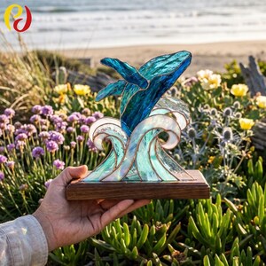 May include: A stained glass sculpture of a whale breaching through ocean waves, crafted with shades of deep blue, light blue, and white glass pieces joined by copper foil, mounted on a rectangular wooden base for display.