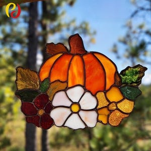 May include: Stained glass pumpkin with a brown stem, orange body, and colorful accents. The pumpkin is surrounded by flowers in shades of white, yellow, and burgundy, and green and gold leaves. A decorative fall-themed item.