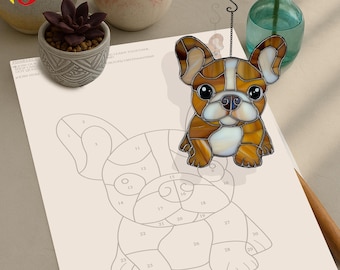 May include: A stained glass French bulldog with brown, white, and tan colors. The bulldog is sitting with its legs crossed and has a happy expression. The stained glass is hanging from a silver chain.