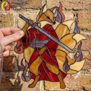 May include: Stained glass fox figure with a sword, in shades of red, orange, and yellow. The fox has multiple tails and is holding a sword. The artwork is held by a silver chain.