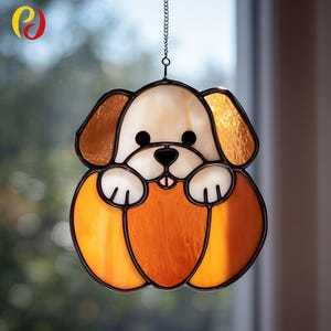 May include: Stained glass dog suncatcher with a black outline. The dog has a cream-colored face and paws, brown ears, and an orange body. A small chain is attached for hanging. Decorative window art.