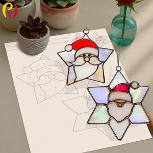 May include: Two star-shaped Christmas ornaments featuring Santa Claus designs. The ornaments have red hats, white beards, and iridescent glass. They are on a white surface with a Santa Claus drawing.
