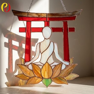 May include: Stained glass panel depicting a meditating figure in white robes, seated on a lotus flower. The figure is set against a red Torii gate. The lotus flower has yellow, orange, and green hues. The panel is designed to hang.