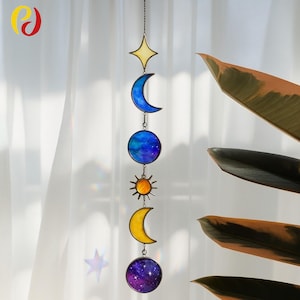 May include: A celestial-themed hanging decoration featuring a star, two crescent moons, a sun, and a sphere. The star is yellow, the moons are blue and yellow, the sun is orange, and the sphere has a blue and purple galaxy design.