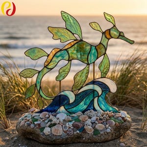 May include: A stained glass leafy seadragon sculpture in shades of green and yellow, mounted on a base of natural stone covered in various seashells and sea glass, featuring a blue and teal stained glass wave element at the bottom.