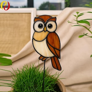May include: A stained glass owl garden stake. The owl features a brown, tan, and cream color scheme with black outlines. The owl is mounted on a black metal stake, perfect for adding a touch of whimsy to any garden or flower pot.
