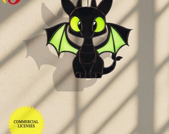 Puede incluir: Dragón de vidrio tintado negro con alas verdes colgando de una cadena. El dragón tiene grandes ojos verdes y una cola pequeña y rizada.