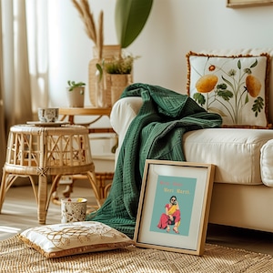 May include: A framed print with a colorful illustration of a woman in a pink and yellow outfit. The text on the print reads "Mera Ghar Meri Marzi". The print is sitting on a white couch with a green throw blanket and a floral pillow.
