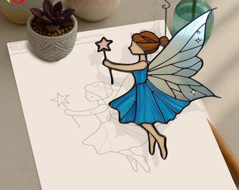 May include: A stained glass fairy in a blue dress and wings, holding a star-shaped wand. The fairy has brown hair and is suspended from a chain. A fairy drawing is on the paper below.