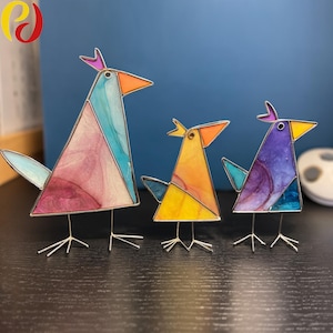 May include: Three decorative bird ornaments with stained-glass effect bodies and wire legs. The birds have triangular bodies in pink, blue, orange, and purple, with orange beaks and purple or yellow crests. A modern home decor item.