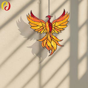 Peut inclure: Un capteur de soleil phénix en vitrail avec une chaîne pour l'accrocher. L'oiseau présente une palette de couleurs vibrantes de rouge, orange et jaune. Les ailes sont déployées et les plumes de la queue tombent vers le bas. Le capteur de soleil est suspendu devant un mur beige.