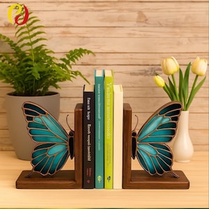 Könnte beinhalten: Buchstützen aus Holz in Schmetterlingsform mit türkisfarbenen und braunen Akzenten. Die Buchstützen halten mehrere Bücher mit farbigen Buchrücken. Ein Farn und Tulpen in einer Vase befinden sich im Hintergrund.