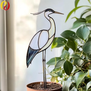 May include: A stained glass heron garden stake. The bird features a white body, black and blue wing, and a long, slender beak. The heron is mounted on a metal stake, perfect for adding a touch of nature to any garden or indoor plant.