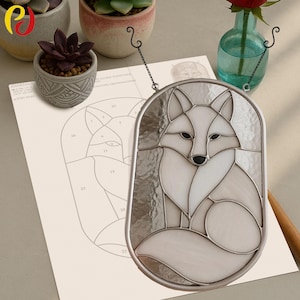 May include: A stained glass fox panel with a silver metal frame. The fox is depicted in white and off-white glass with black accents. A paper pattern with a fox outline is visible in the background. The panel is hanging from a chain.