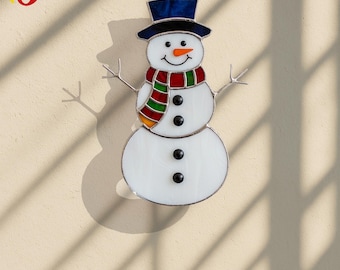 May include: A stained glass snowman decoration with a blue top hat, a colorful scarf, and a smiling face. The snowman has three black buttons and twig arms. A festive winter holiday decoration.