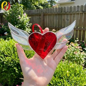 May include: A stained glass heart with iridescent wings, featuring a vibrant red heart shape. The wings are clear with an iridescent sheen, and a red ribbon is attached for hanging. This decorative piece is perfect for Valentine's Day or as a unique home decor item.