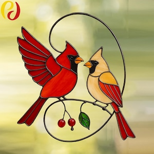 Op de afbeelding: Een hangend glas-in-loodraam toont twee rode kardinaals, die op een tak zitten met groene bladeren en rode bessen. De kardinaals kijken elkaar aan en lijken verliefd te zijn.
