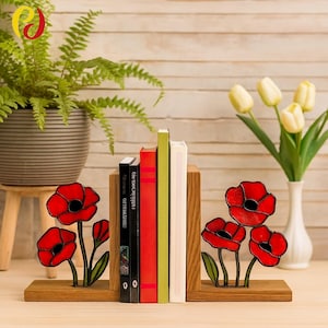 Può includere: Reggilibri in legno con disegni di fiori di papavero rossi. I reggilibri sostengono una pila di libri con dorsi rossi, verdi, neri e bianchi. Una pianta in vaso e un vaso di tulipani gialli sono sullo sfondo.