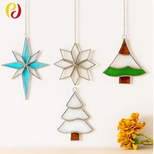May include: Stained glass Christmas ornaments in star and tree shapes. The star ornaments are blue and white, and the tree ornaments are green, white, and brown. Each ornament hangs from a silver chain.