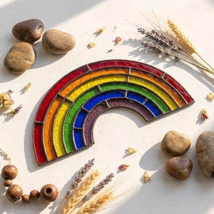 Può includere: Un acchiappasole arcobaleno in vetro colorato con fasce arcuate di vetro rosso, arancione, giallo, verde, blu e viola unite da linee di saldatura in metallo scuro, disposte in una forma semicircolare con una finitura liscia e traslucida.