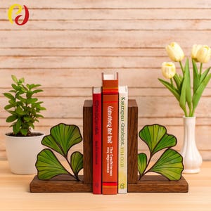 May include: Dark wooden bookends with a leaf design, holding three books with red, orange, and white spines. A small potted plant and a vase of yellow tulips are on either side. The bookends are made of dark wood.