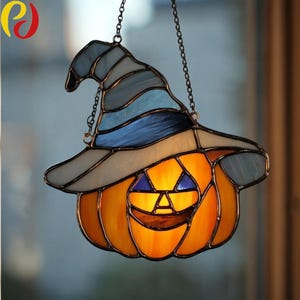 May include: Stained glass Halloween decoration featuring a smiling jack-o'-lantern wearing a witch's hat. The pumpkin is orange with a glowing interior, and the hat is blue, gray, and white. The piece hangs from a chain.
