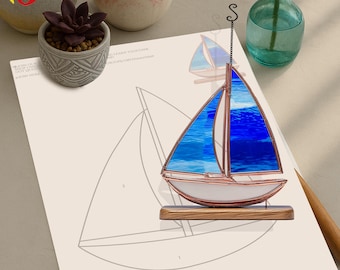 Puede incluir: Un velero de vitral con un diseño azul y blanco, montado sobre una base de madera. El velero está colgado de una cadena y está rodeado de un fondo blanco.