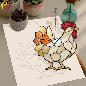 Peut inclure: Un coq en verre coloré avec une crête et des barbillons rouges, des plumes brunes et orange et un corps blanc. Le coq est suspendu à une ficelle noire et est placé au-dessus d'un motif numéroté.