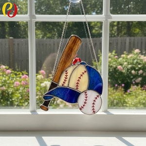 Könnte beinhalten: Baseball-Suncatcher aus Glas mit Baseballschläger, Baseballkappe und Baseball. Die Kappe ist blau und cremefarben mit roten Nähten, der Baseball ist weiß mit roten Nähten. Der Schläger ist braun.