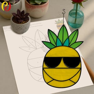 Può includere: Un ananas in vetro colorato con un designo nero e giallo. L'ananas indossa occhiali da sole e ha una cima verde e frondosa. L'ananas è appeso a una corda.