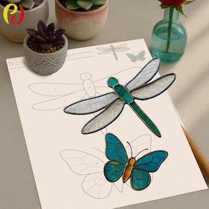 May include: A stained glass dragonfly and butterfly sit atop a paper with dragonfly and butterfly outlines. The dragonfly has white wings and a green body. The butterfly is blue and yellow. A pencil and small potted plants are also visible.