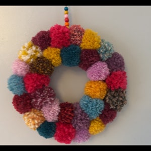 May include: A colorful pom-pom wreath with a variety of colors including pink, purple, red, yellow, teal, brown, and white.