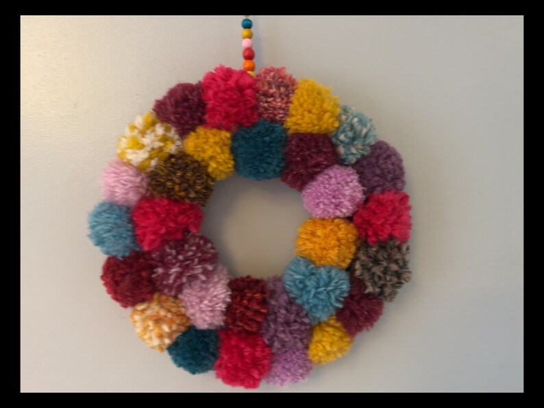 May include: A colorful pom-pom wreath with a variety of colors including pink, purple, red, yellow, teal, brown, and white.