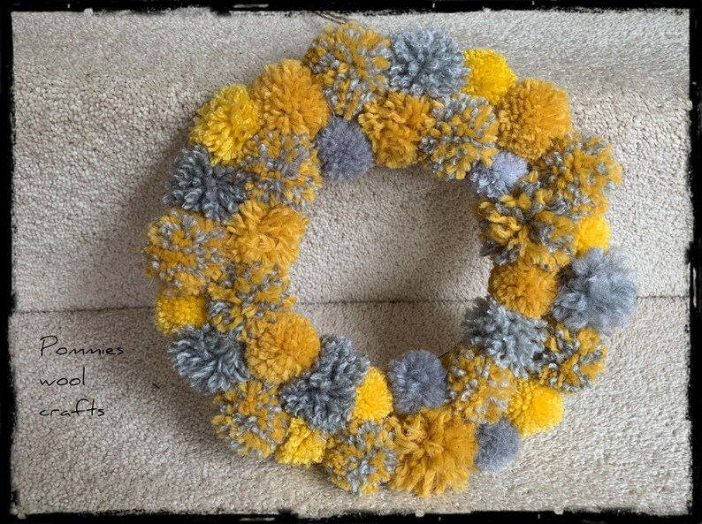 May include: A wreath made of yellow and gray pom-poms. The wreath is hanging on a wall.