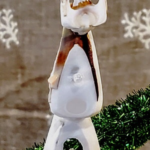 May include: A handcrafted seashell decoration featuring a star-shaped top and a series of white and brown shells. The ornament is adorned with a green garland and a shimmering green ribbon.