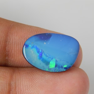 May include: A polished, oval-shaped blue opal gemstone featuring vibrant flashes of green and lighter blue color play across its smooth, reflective surface. The stone displays a deep, saturated blue base color with distinct iridescent inclusions.