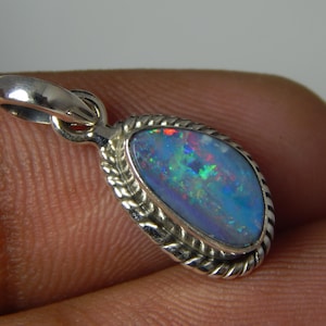 May include: A teardrop-shaped pendant with a vibrant opal gemstone. The opal displays a mix of blue, green, and red colors. The pendant is set in a silver-colored metal with a braided rope design around the stone. The bail is also silver.