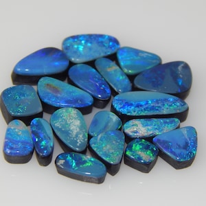 May include: A collection of loose, polished black opals featuring vibrant blue and green flashes of color. Each gemstone has a smooth, rounded, or irregular shape with a dark base, showcasing a play of color across the surface of the stones.