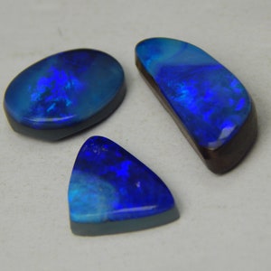 Può includere: Tre pietre preziose di opale lucide nelle tonalità del blu e del verde acqua. Gli opali hanno un retro grigio scuro e sono di forma ovale, curva e triangolare. Gli opali mostrano un vibrante gioco di colori, con lampi di blu e verde.
