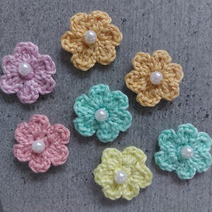 Può includere: Sette fiori fatti a mano all'uncinetto in colori pastello: rosa, giallo, azzurro e lavanda. Ogni fiore ha una perla bianca al centro. Questi fiori decorativi sono ideali per l'artigianato e gli abbellimenti.