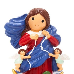 May include: A figurine of the Virgin Mary, depicted in a blue robe with a white rope, holding the rope in her hands. Two angels are on either side of her, holding the rope. The figurine is standing on a crescent moon with a green snake wrapped around it.