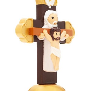 May include: A brown wooden cross with a gold base. A white figure of Jesus is on the cross with a dove above. A white figure of God is behind Jesus with his arms around Jesus.