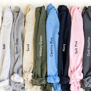 Puede incluir: Una selecci&oacute;n de diez camisetas dobladas en varios colores, incluyendo blanco, ceniza, gris deportivo, arena, verde militar, azul Carolina, azul marino, rosa suave, gris oscuro y negro.