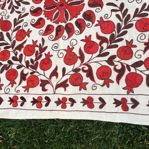 May include: White fabric with red and brown embroidery of pomegranates and leaves. The fabric has a border of red and brown embroidery.