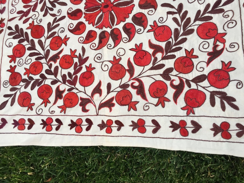 May include: White fabric with red and brown embroidery of pomegranates and leaves. The fabric has a border of red and brown embroidery.